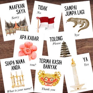 May include: A collection of white cards with Indonesian phrases and their English translations. Each card features watercolor illustrations of various objects, including a flag, a lizard, and a traditional building. The cards are arranged on a wooden surface.