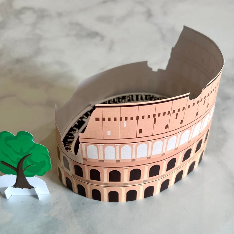 May include: A paper model of the Colosseum in Rome, Italy. The model is made of brown and white paper and is partially assembled. The model is missing a section of the top, revealing the interior of the structure.
