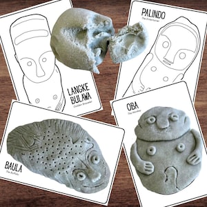 May include: A selection of grey, textured sculptures and illustrated cards. The cards display line drawings of faces and figures with text labels. The sculptures are shaped like faces and figures. The text on the cards includes "Lange Bulawa", "Palindo", "Baula", and "Oba".