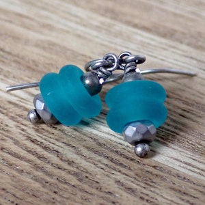 May include: A pair of turquoise blue glass bead earrings with silver wire and metal accents.