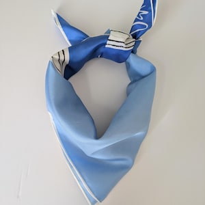 May include: A silk scarf in shades of blue, tied in a knot. The scarf features a light blue base with darker blue accents and white trim. The design includes a white and black striped section.