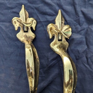 May include: A pair of ornate brass door handles with a fleur-de-lis design. The handles are polished and have a shiny finish.