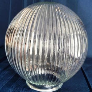 May include: A clear, ribbed glass globe with a round shape. The globe has vertical ridges and a small base. The glass is transparent, allowing light to pass through. This decorative piece is suitable for lighting fixtures.