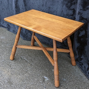 May include: A wooden coffee table with a rectangular top and four turned legs. The legs are connected by a cross-shaped stretcher.