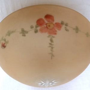 May include: A vintage, frosted glass light fixture with a floral design. The fixture is a soft peach color and features a hand-painted design of a large pink flower with green leaves and small red roses. A starburst pattern is at the bottom.