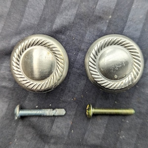 May include: Two silver-toned round cabinet knobs with a decorative grooved design. Two silver screws are included.