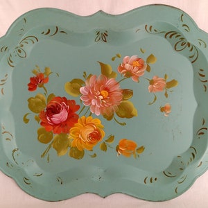 May include: A vintage, teal-colored metal serving tray with a hand-painted floral design. The flowers are in shades of pink, red, yellow, and orange. The tray has a scalloped edge and a gold-painted border.