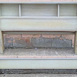 May include: A light green wooden headboard with a built-in shelf and two compartments. The headboard is attached to a matching footboard. The furniture has a distressed finish and is set against a brick wall.