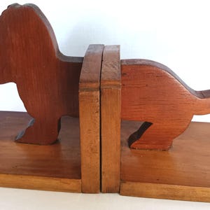 May include: Wooden dachshund bookends in a warm brown finish. The bookends are shaped like a dachshund dog, with the body and legs carved from wood. The bookends are designed to hold books upright on a shelf or desk.