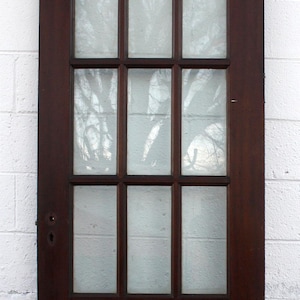 May include: A dark brown wooden door with a 9-pane glass window. The glass is frosted and the panes are separated by thin wooden strips.