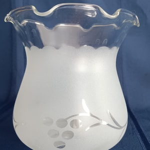 May include: A clear glass lampshade with a frosted body and a ruffled top edge. The frosted surface features a silver grape vine design. The lampshade has a rounded shape and a small base.