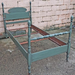 May include: A vintage twin-size bed frame painted in a teal-green hue. The headboard features a decorative, curved top, and the footboard has a spindle design. The bed frame is made of wood and has a classic, antique aesthetic.