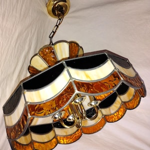 May include: A stained glass ceiling light fixture with a black, white, and amber design. The fixture has a chain and a brass ceiling mount.