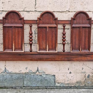 Pu&ograve; includere: Una testiera in legno vintage con finitura marrone scuro. La testiera presenta tre pannelli ad arco con doghe verticali e fusi decorativi. I pali hanno pinnacoli. La testiera &egrave; larga circa 152 cm.