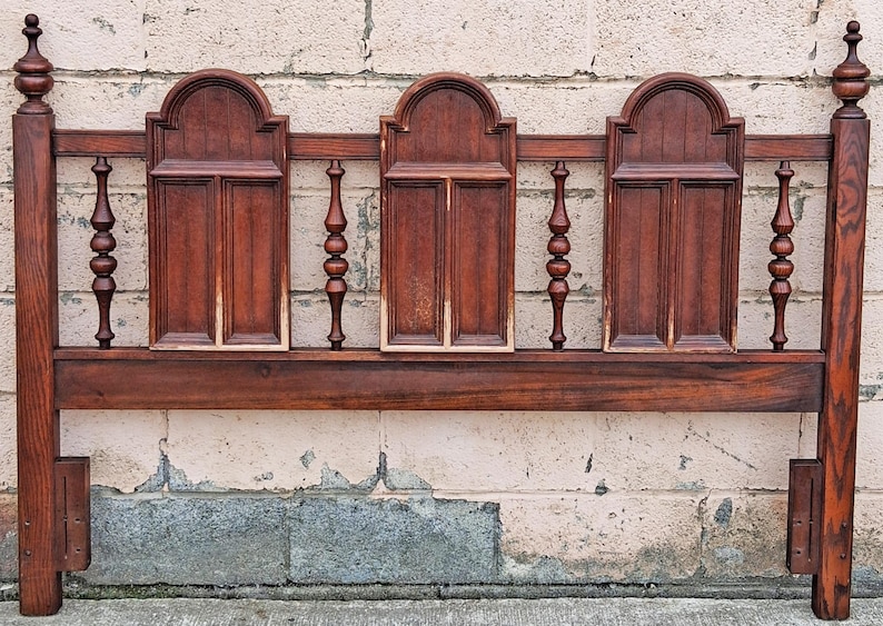 Pu&ograve; includere: Una testiera in legno vintage con finitura marrone scuro. La testiera presenta tre pannelli ad arco con doghe verticali e fusi decorativi. I pali hanno pinnacoli. La testiera &egrave; larga circa 152 cm.