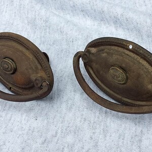 May include: Two antique oval-shaped door pulls with a decorative ring handle. The pulls are made of metal and have a dark brown patina.