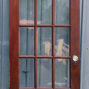 May include: A rectangular wooden door with a dark brown finish featuring nine glass panes arranged in a three-by-three grid. The door includes a clear, faceted glass doorknob and a black metal keyhole plate mounted on the right side of the frame.