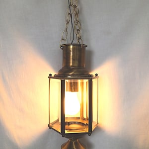 May include: A brass pendant light fixture with a clear glass shade and a chain hanging from the ceiling. The light is on and illuminating the room.