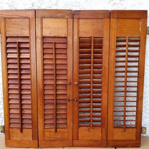 May include: Four connected wooden shutters with a medium brown finish, featuring horizontal slats and a vertical central bar on each panel. The shutters include small round wooden knobs and a metal latch mechanism for securing the panels together.