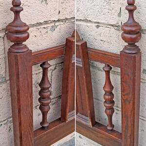 Pu&ograve; includere: Primo piano di una testiera di letto in legno vintage. La testiera &egrave; realizzata in legno marrone scuro con fusi e pinnacoli torniti e ornati. La cornice ha un design classico e antico, che mostra le venature del legno e l'artigianato. La testiera &egrave; contro un muro strutturato di colore chiaro.