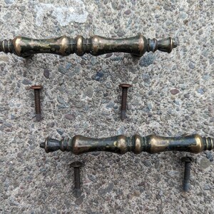 Puede incluir: Dos tiradores de puerta de armario de latón antiguo con detalles ornamentados y cuatro tornillos a juego.