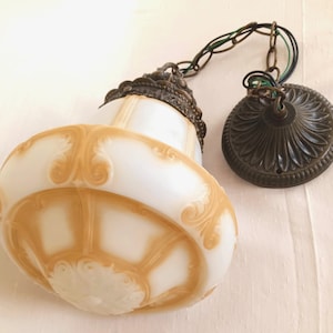 May include: A white and brown glass pendant light fixture with a decorative metal chain and a bronze-colored metal ceiling plate.