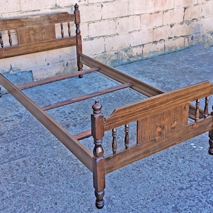 May include: A vintage wooden bed frame with a dark brown finish. The headboard and footboard feature decorative carved details and turned posts. The bed frame is designed for a twin-sized mattress, with a length of approximately 75 inches.