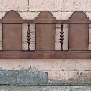 Pu&ograve; includere: Una testiera in legno vintage con finitura marrone scuro. La testiera presenta un design rettangolare con tre pannelli ad arco e fusi decorativi. I pali sono sormontati da pinnacoli, aggiungendo un tocco classico ai mobili della camera da letto.