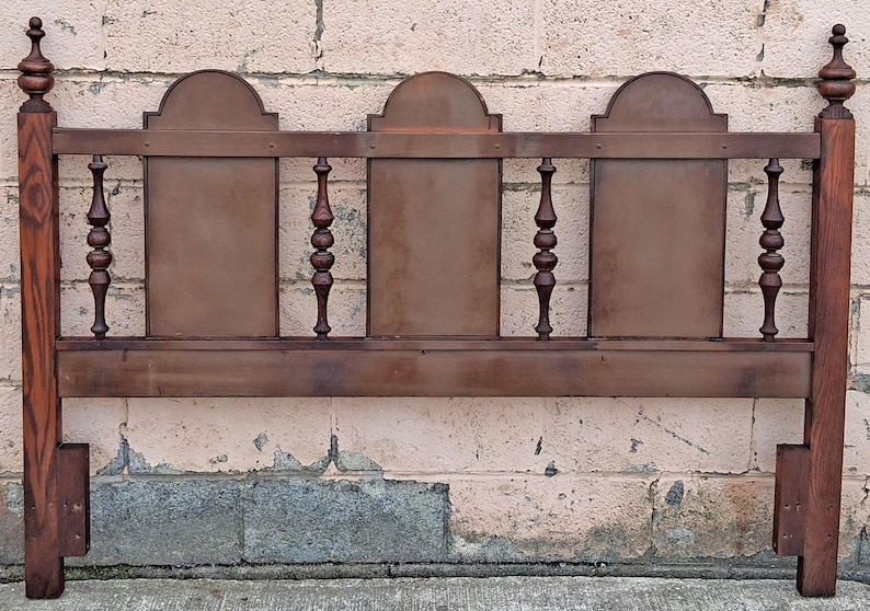 Pu&ograve; includere: Una testiera in legno vintage con finitura marrone scuro. La testiera presenta un design rettangolare con tre pannelli ad arco e fusi decorativi. I pali sono sormontati da pinnacoli, aggiungendo un tocco classico ai mobili della camera da letto.