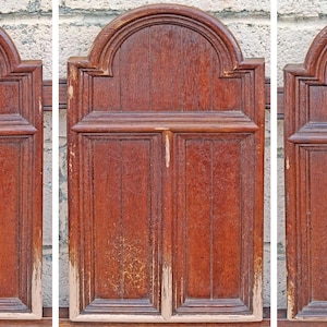 Pu&ograve; includere: Tre pannelli in legno antichi con finitura marrone-rossastra. Ogni pannello presenta un design rettangolare con assi di legno verticali e una parte superiore ad arco. I pannelli mostrano segni di usura, con alcune aree con perdita di vernice.