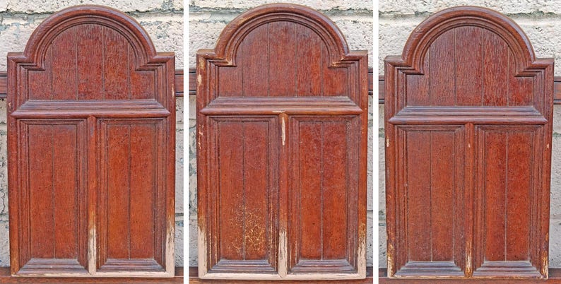 Pu&ograve; includere: Tre pannelli in legno antichi con finitura marrone-rossastra. Ogni pannello presenta un design rettangolare con assi di legno verticali e una parte superiore ad arco. I pannelli mostrano segni di usura, con alcune aree con perdita di vernice.