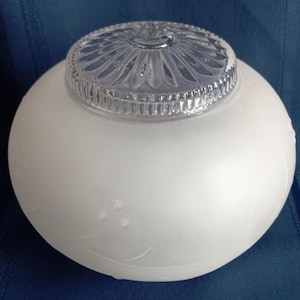 May include: A white, frosted glass globe light fixture with a clear, patterned glass top. The globe has a round shape with a floral design etched on the surface. The fixture is designed for ceiling or wall mounting.