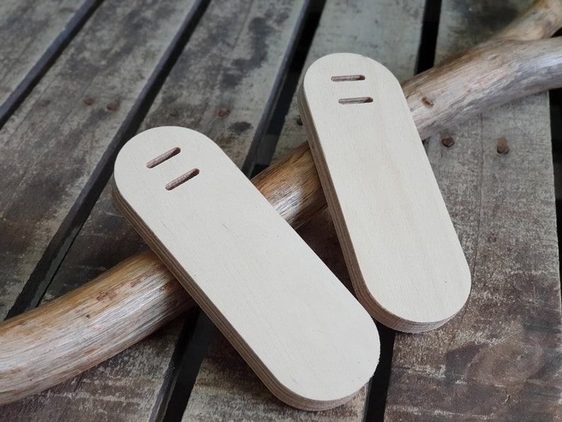 May include: Two unfinished wooden oval-shaped pieces with two holes each. The pieces are lying on a wooden surface.