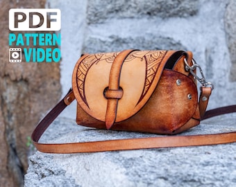 May include: A brown leather crossbody bag with a decorative design on the front flap. The bag has a strap and a metal clasp. The bag is sitting on a stone surface.