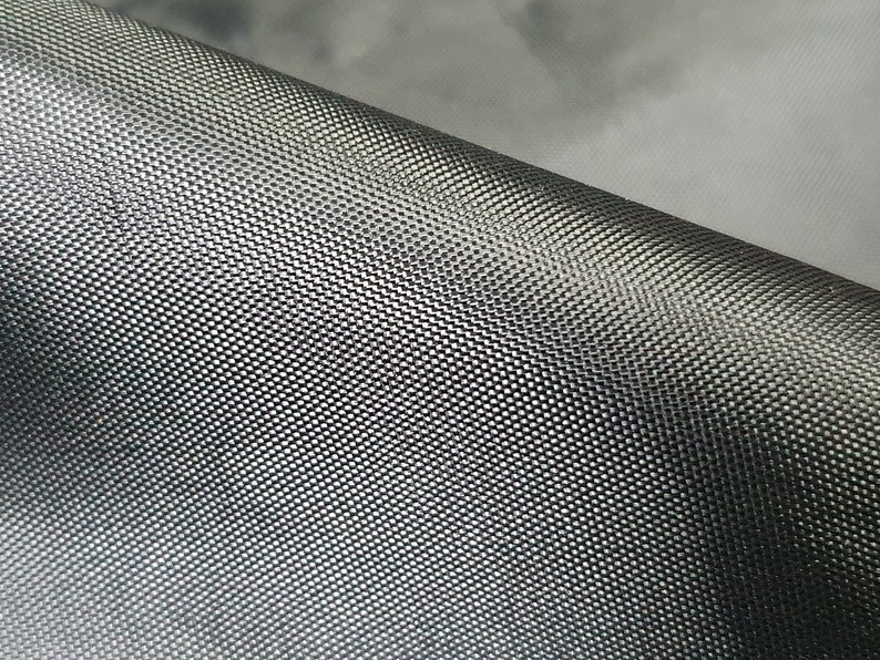Pode incluir: Close-up de um tecido preto com um padr&atilde;o tecido texturizado. O tecido tem um brilho sutil e um design ligeiramente elevado, semelhante a um favo de mel.