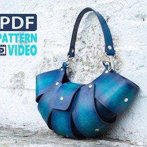 Puede incluir: Un bolso de mano de cuero azul hecho a mano con un diseño único en capas. El bolso presenta una forma curva, un asa superior y herrajes plateados. El texto "PDF PATTERN VIDEO" es visible en la esquina superior izquierda.