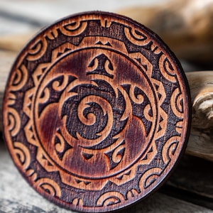 Puede incluir: Un posavasos redondo de madera con una mancha marrón oscura y un diseño tallado de una tortuga con detalles intrincados. El posavasos tiene un patrón circular alrededor del borde.
