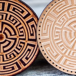 Könnte beinhalten: Zwei runde Holz-Untersetzer mit geometrischem Muster. Ein Untersetzer hat ein schwarz-braunes Design, während der andere ein hellbraunes Design hat.