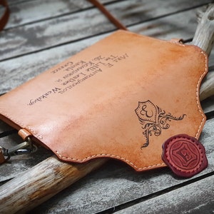May include: A tan leather crossbody bag with a decorative seal and the text "The Little Leather Workshop. MR. E ANTONOPOULOU 26. KOMNINON S Kamla. GREECE" engraved on the front.