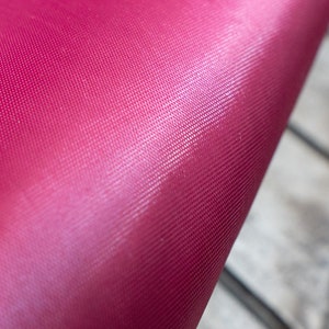 Pode incluir: Close-up de um tecido rosa brilhante com um padr&atilde;o texturizado sutil. O tecido &eacute; liso e tem um leve brilho.
