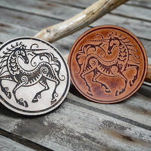 May include: Two round wooden coasters featuring a black and white and a brown and white unicorn design. Both coasters are circular and have a raised edge.