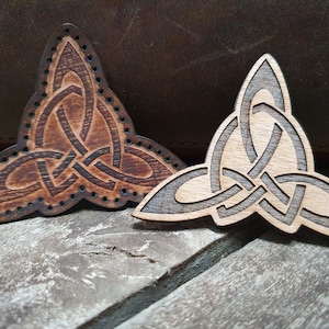 May include: Two wooden Celtic knot triquetra designs. One is a dark brown color and the other is a light brown color.
