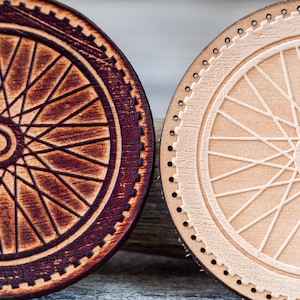 Op de afbeelding: Twee houten onderzetters met fietswieldesigns. Eén onderzetter is donkerbruin gebeitst, de andere heeft een natuurlijke lichte houtkleur. Beide hebben gedetailleerde spaak- en velgpatronen. Perfect voor fietsliefhebbers.