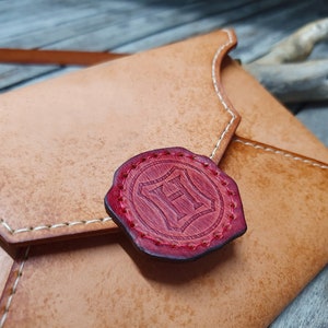 May include: A tan leather envelope with a red wax seal featuring the letter "H" in a shield design.