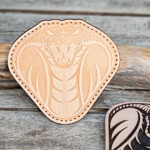 Peut inclure: Un patch en cuir brun clair avec une sculpture détaillée d'un cobra serpent avec la bouche ouverte. Le patch a une bordure cousue.
