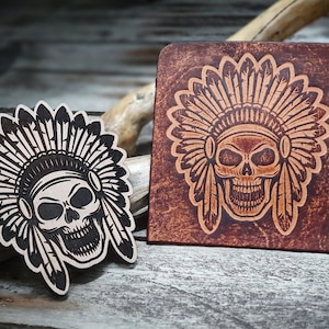 Op de afbeelding: Twee leren patches met een schedel die een indiaanse hoofdtooi draagt. De hoofdtooi is bruin op de linker patch en oranje op de rechter patch. De schedel is zwart op de linker patch en bruin op de rechter patch.