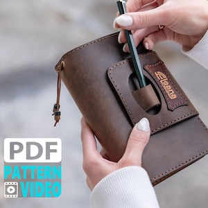 May include: A brown leather notebook cover with a pen holder and a leather strap. The cover has the text "Eleana Workshop" embossed on it.