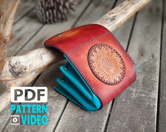 May include: A brown leather wallet with a sunflower design and a turquoise blue interior. The wallet is folded closed and is sitting on a wooden surface.
