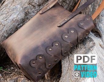 May include: A brown leather tote bag with heart-shaped cutouts along the side. The bag has two handles and is secured with rivets. The bag is sitting on a weathered wooden surface. The image also contains the text "PDF PATTERN VIDEO".