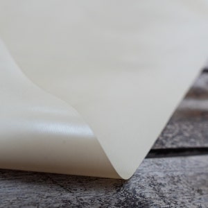 Pode incluir: Close-up de uma superf&iacute;cie de tecido branco lisa dobrada sobre si mesma. O tecido est&aacute; sobre uma superf&iacute;cie de madeira.